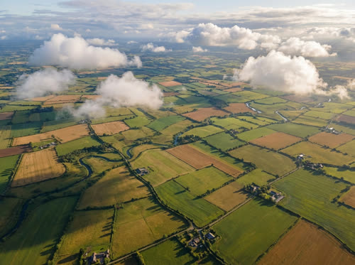 Beautiful farmland meadows and fields from an aerial view, with just a few single clouds drifting overhead. We are flying above the clouds.